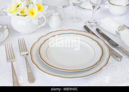 Classic serving for a gala dinner with luxurious porcelain, silverware and spring flowers on a white tablecloth Stock Photo
