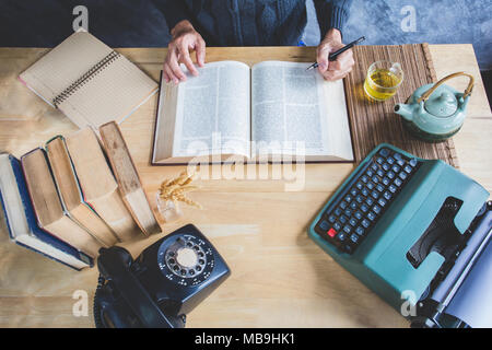 Journalist sitting at the table and making notes in book with tea cup and accessories Stock Photo