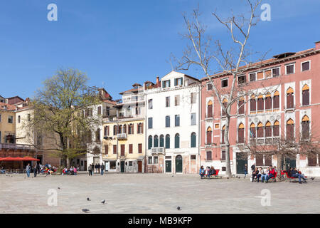 Campo San Polo, San Polo, Venice, Veneto, Italy in spring with local Venetians relaxing on benches in the sunshine under trees Stock Photo