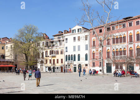 Campo San Polo, San Polo, Venice, Veneto, Italy in spring with locals and tourists relaxing on benches  and crossing the square in front of palazzos Stock Photo