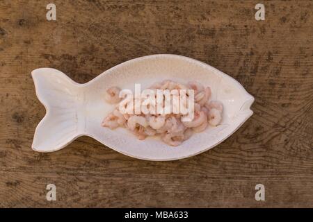 Seafood concept. Raw shrimps in a fish shaped plates on rustic wooden tabletop. Stock Photo
