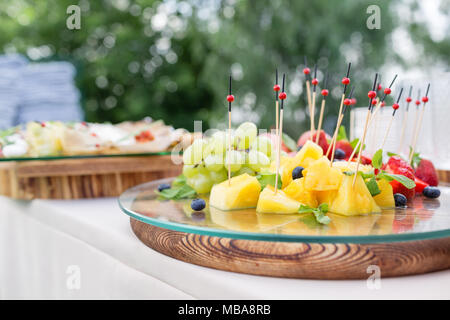 Wooden plate with sliced fruits and berries on a buffet table. Summer party outdoor. Horizontal photo Stock Photo