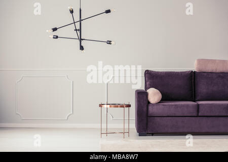 Copper coffee table next to a purple couch with roll pillows in a living room interior with wall molding Stock Photo