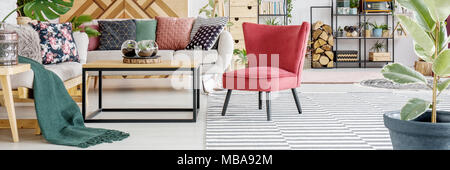 Green blanket on sofa and red chair next to table in cosy living room interior with ficus Stock Photo