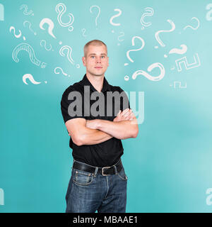 Concept of preoccupied and thoughtful man with folded arms being confused and looking for solution for a problem symbolized by question marks around h Stock Photo