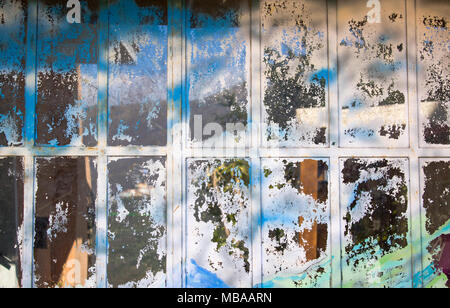 Old glass surface stained with torn posters and spray painted colors abstract background. Stock Photo