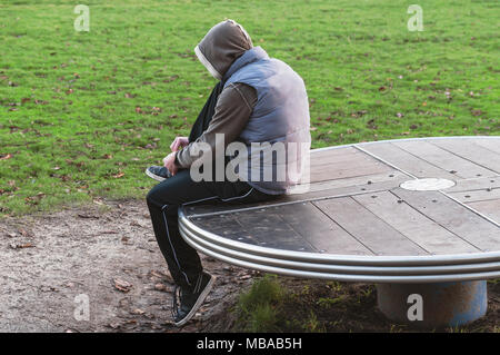 boy with sweatpants and waistcoat sits on a table to fasten his shoe laces Stock Photo