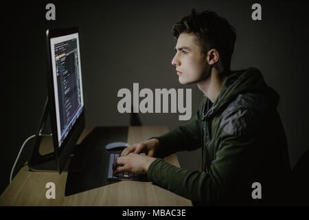 Handsome male programmer, IT person, hacker, works in computer on internet, black background. Stock Photo