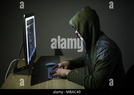 A hacker in a hood on a dark background hacking computer networks Stock Photo