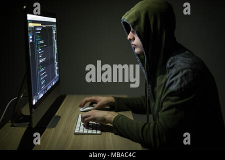 Man wearing hoodie hacking server in dark room Stock Photo