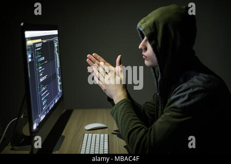 Hacker in glasses breaking code. Criminal hacker penetrating network system from his dark hacker room. Stock Photo