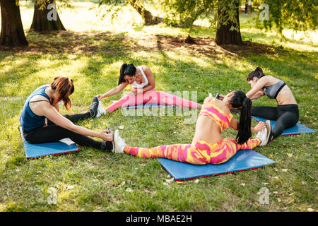 Four beautiful motivated female friends doing stretching exercise in the city park. Stock Photo