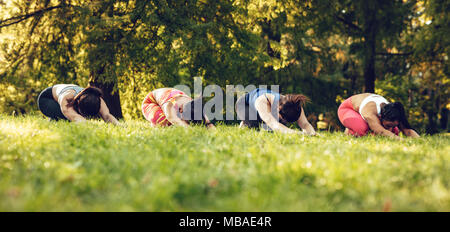 Four beautiful motivated female friends doing stretching exercise in the city park. Stock Photo