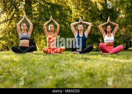 Fitness group of four young women doing yoga meditation in the city park. Stock Photo