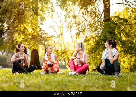 Four beautiful motivated female friends relaxing after training in the city park. Stock Photo