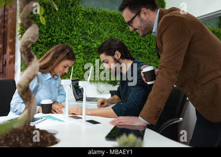 Smart qualified skilled young engineers looking at the project of alternative energy with miniatures of windmill turbines at the table. Stock Photo