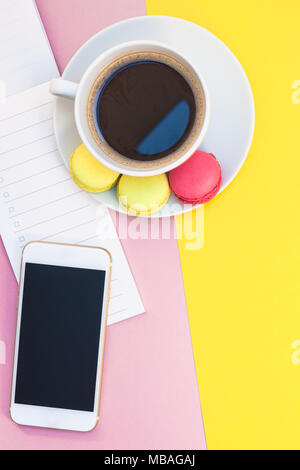 Creative flat lay photo of coffee cup with macaroons and a notepad with copy space on pink and yellow background minimal style Stock Photo