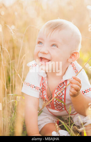 9 month old infant baby portrait. Cute funny emotional little child sitting in golden wheat field alone. Closeup of blond boy's face with happy beauti Stock Photo