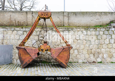 old orange and rusty Crane bucket in front of a wall Stock Photo