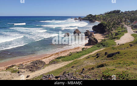 breaking waves through rocks onto sandy beach with green vegetation Stock Photo