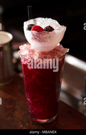 vertical shot of an intense red cocktail on a bar counter with an ice cup and berries in it as decoration.Cocktail has been made with organic fruit Stock Photo