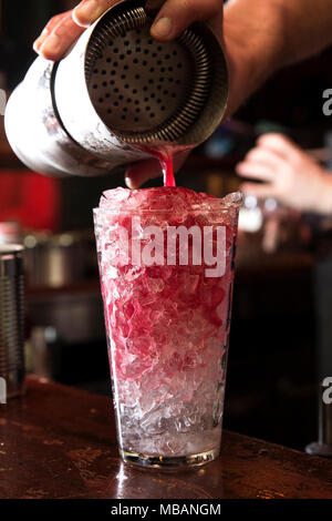 closeup of a barman making a red cocktail, pouring it into its glass full of crushed ice. Stock Photo