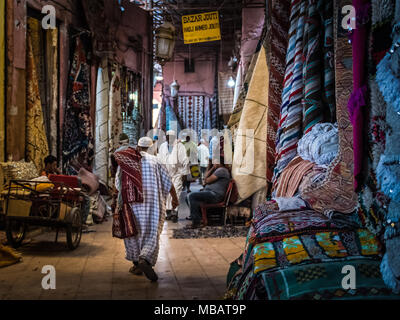 Numerous colourful carpets hang from the ceiling in the Marrakech carpet market in Morocco. Moroccan men walk, sit & stand in the market. Stock Photo