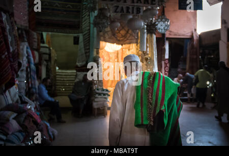 A moroccan man walks with a green and red carpet slung over his shoulder in the Marrakech carpet market in Morocco. Stock Photo