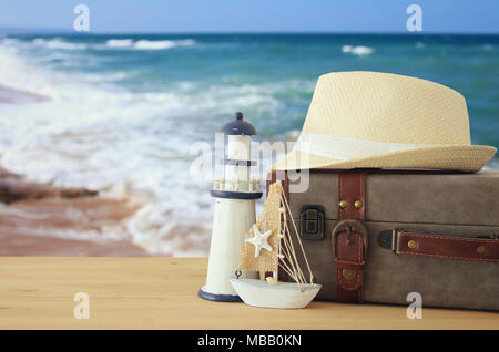 traveler vintage luggage, boat and fedora hat over wooden table infront of sea landscape. holiday and vacation concept Stock Photo