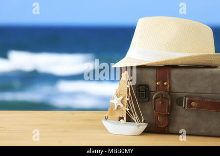 traveler vintage luggage, boat and fedora hat over wooden table infront of sea landscape. holiday and vacation concept Stock Photo