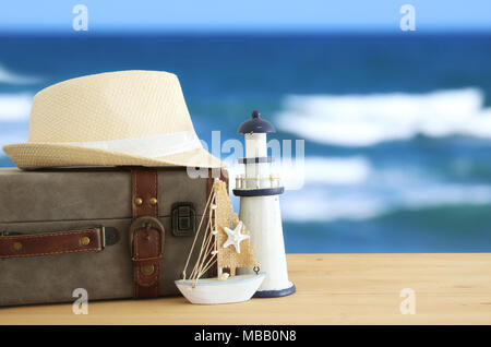 traveler vintage luggage, boat and fedora hat over wooden table infront of sea landscape. holiday and vacation concept Stock Photo