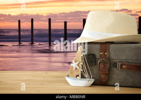 traveler vintage luggage, boat and fedora hat over wooden table infront of sea landscape. holiday and vacation concept Stock Photo