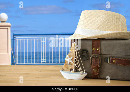 traveler vintage luggage, boat and fedora hat over wooden table infront of sea landscape. holiday and vacation concept Stock Photo