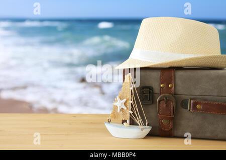 traveler vintage luggage, boat and fedora hat over wooden table infront of sea landscape. holiday and vacation concept Stock Photo