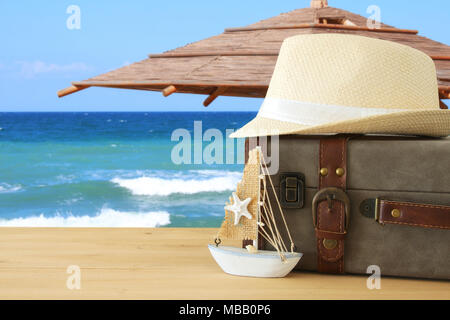 traveler vintage luggage, boat and fedora hat over wooden table infront of sea landscape. holiday and vacation concept Stock Photo