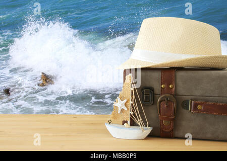 traveler vintage luggage, boat and fedora hat over wooden table infront of sea landscape. holiday and vacation concept Stock Photo