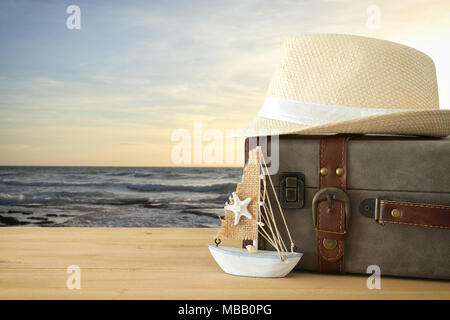 traveler vintage luggage, boat and fedora hat over wooden table infront of sea landscape. holiday and vacation concept Stock Photo