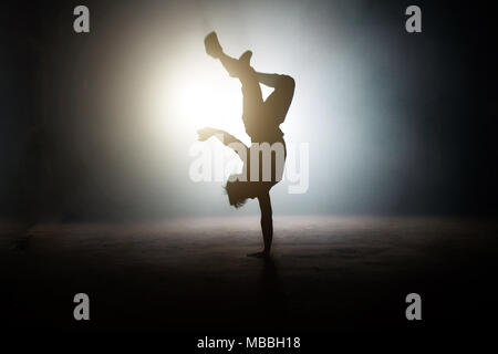 man showing a one-handed handstand with legs on the bright stage Stock Photo