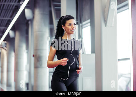 woman with earphones running on indoor track at gym Stock Photo
