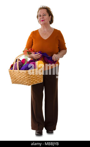 Attractive senior woman holding a basket of brightly colored balls of wool for knitting in a full length portrait on white Stock Photo