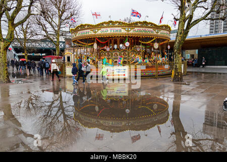 A fairground carousel on the South Bank of the River Thames in London, reflected in a pool of rain water.