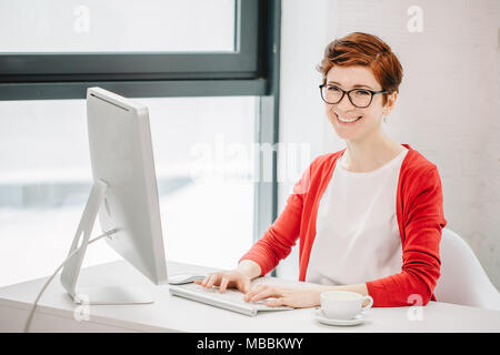 businesswoman working on computer and looking at camera in office Stock Photo