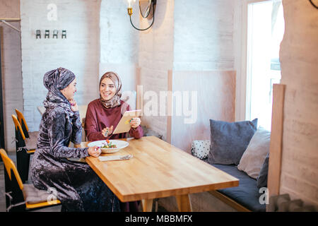 Two Muslim women in cafe, shop online using electronic tablet Stock Photo