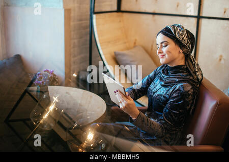 beautiful Arabic Muslim girl using tablet in cafe Stock Photo