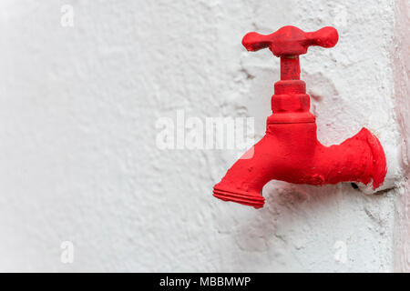 Metallic faucet painted red on a rough white wall. Free space to put text Stock Photo