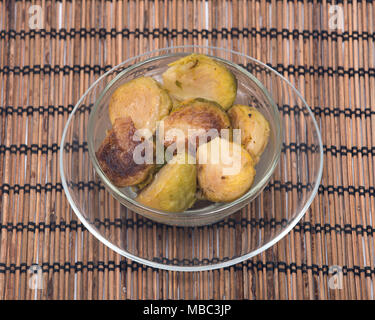 Roasted brussels sprouts in clear glass dish on bamboo placemat Stock Photo