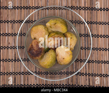 Roasted brussels sprouts in clear glass dish on bamboo placemat Stock Photo