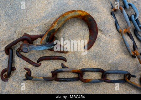 Rusty and corroded mooring ring, chain and shackle lying in the sand on the beach in th harbour gat st Ives on the Cornish coastline.