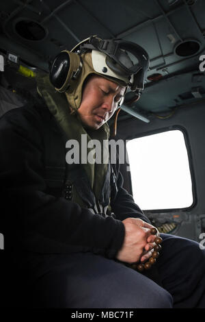 ARABIAN GULF (Feb. 14, 2018) Lt. Long Nguyen, a chaplain assigned to the aircraft carrier USS Theodore Roosevelt (CVN 71), prays during “Holy Helo” operations in an MH-60S Sea Hawk, assigned to the Indians of Helicopter Sea Combat Squadron (HSC) 6. Theodore Roosevelt and its carrier strike group are deployed to the U.S. 5th Fleet area of operations in support of maritime security operations to reassure allies and partners and preserve the freedom of navigation and the free flow of commerce in the region. (U.S. Navy Stock Photo