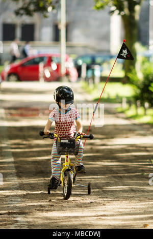 A young boy wearing a helmet riding a bike with training wheels and a flag, on a sidewalk in Berlin, Germany. Stock Photo